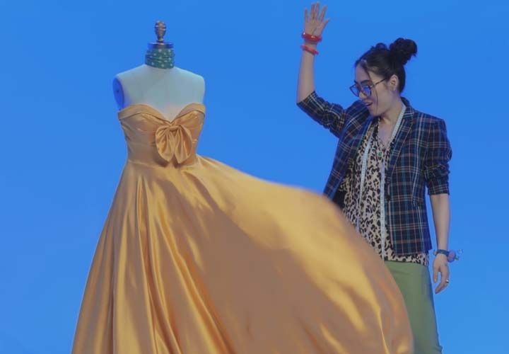 a fashion designer standing next to a dress in front of a blue background