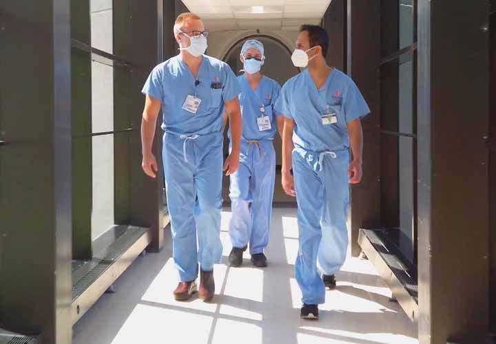 three doctors in scrubs and masks walking down a hallway