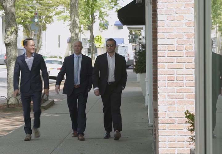 three men in suits walking down a sidewalk in the Hamptons
