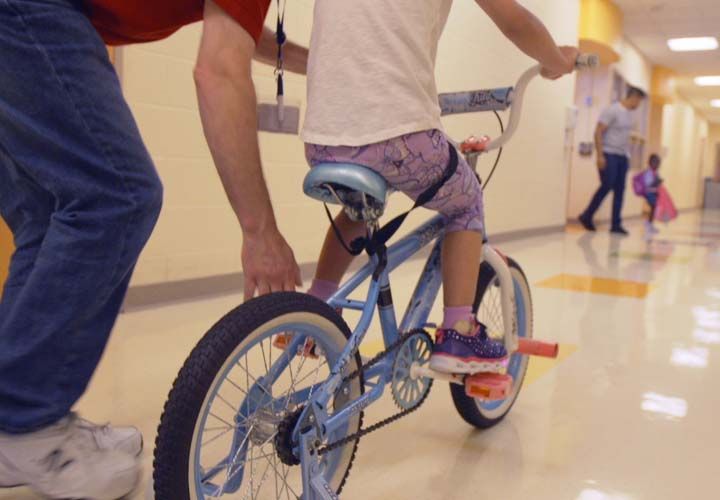 a girl on a bicyle in a hallway being pushed by her father