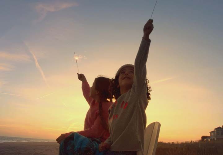 two girls at the beach at sundown holding sparklers in the air