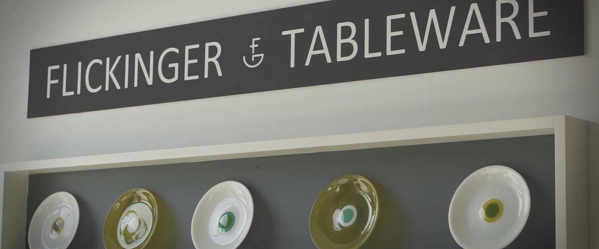 a grey wall with a plates displayed and a sign for Flickinger Tableware