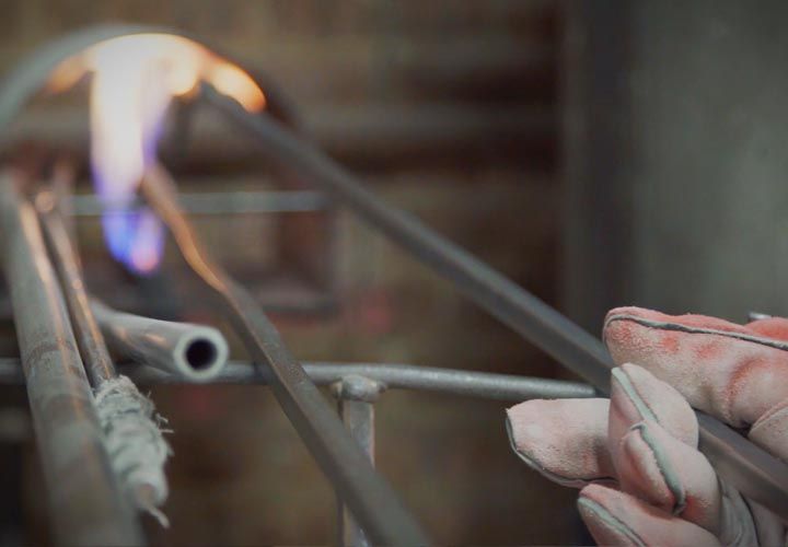 a man holding glass making tools into an open fired oven