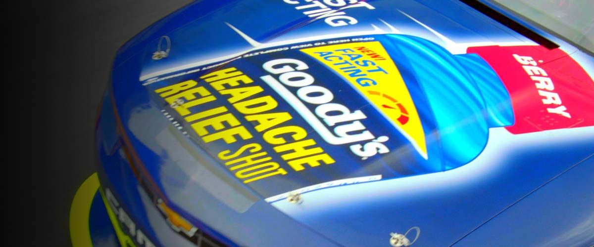 the hood of a blue racecar driving on a racetrack with a bottle of Goody's Headache Relief Shot painted on it