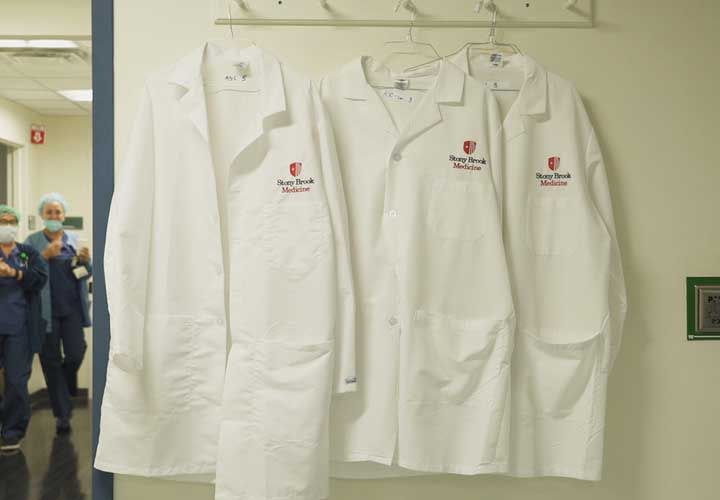 three white doctors jackets hanging on a hook