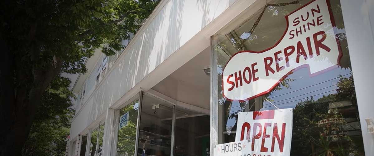 storefront of a cobblers store with a shoe repair sign in the window